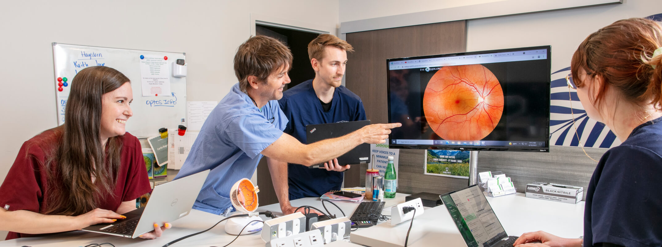A group of medical professionals in scrubs collaborate in a meeting room, discussing a detailed retinal image displayed on a large screen.