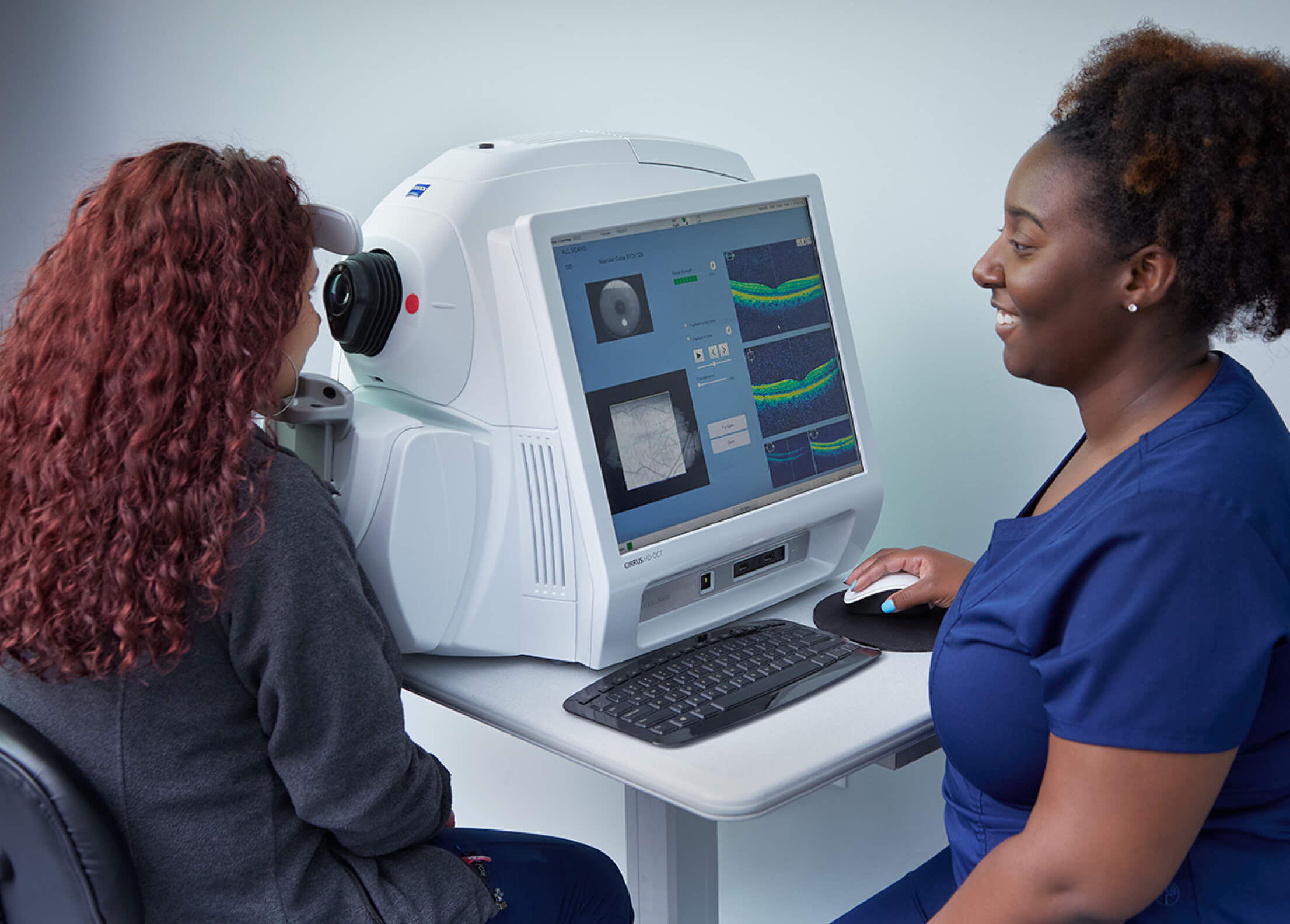 A medical professional in navy scrubs assists a patient undergoing an eye scan using an advanced diagnostic machine.